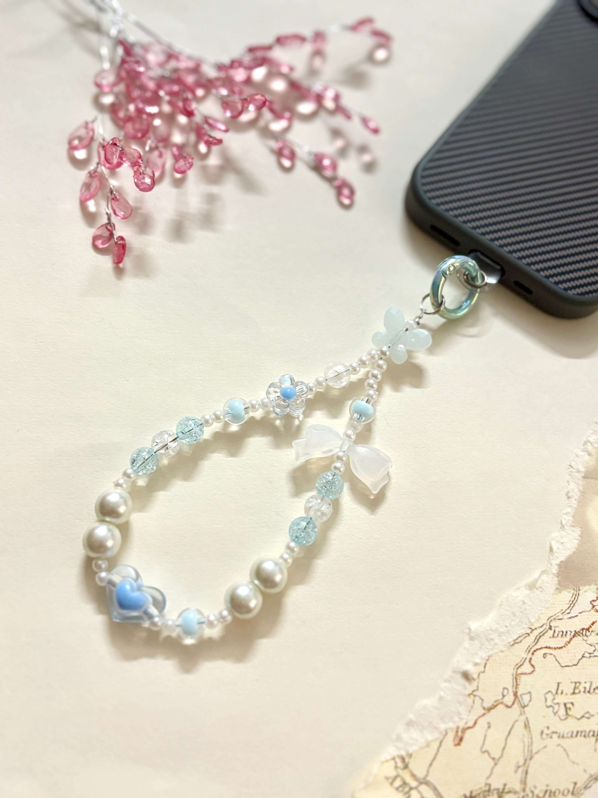 Decorative beaded phone charm featuring heart, flower, and pearl-like beads with a mix of textures and finishes, designed as a stylish phone strap accessory.