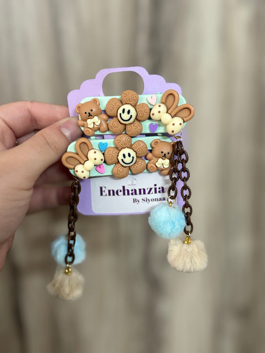 Cute chocolate-themed hair clips with smiling flowers, teddy bears, and bunnies. Dangling pastel pom-poms add a playful flair to your look.