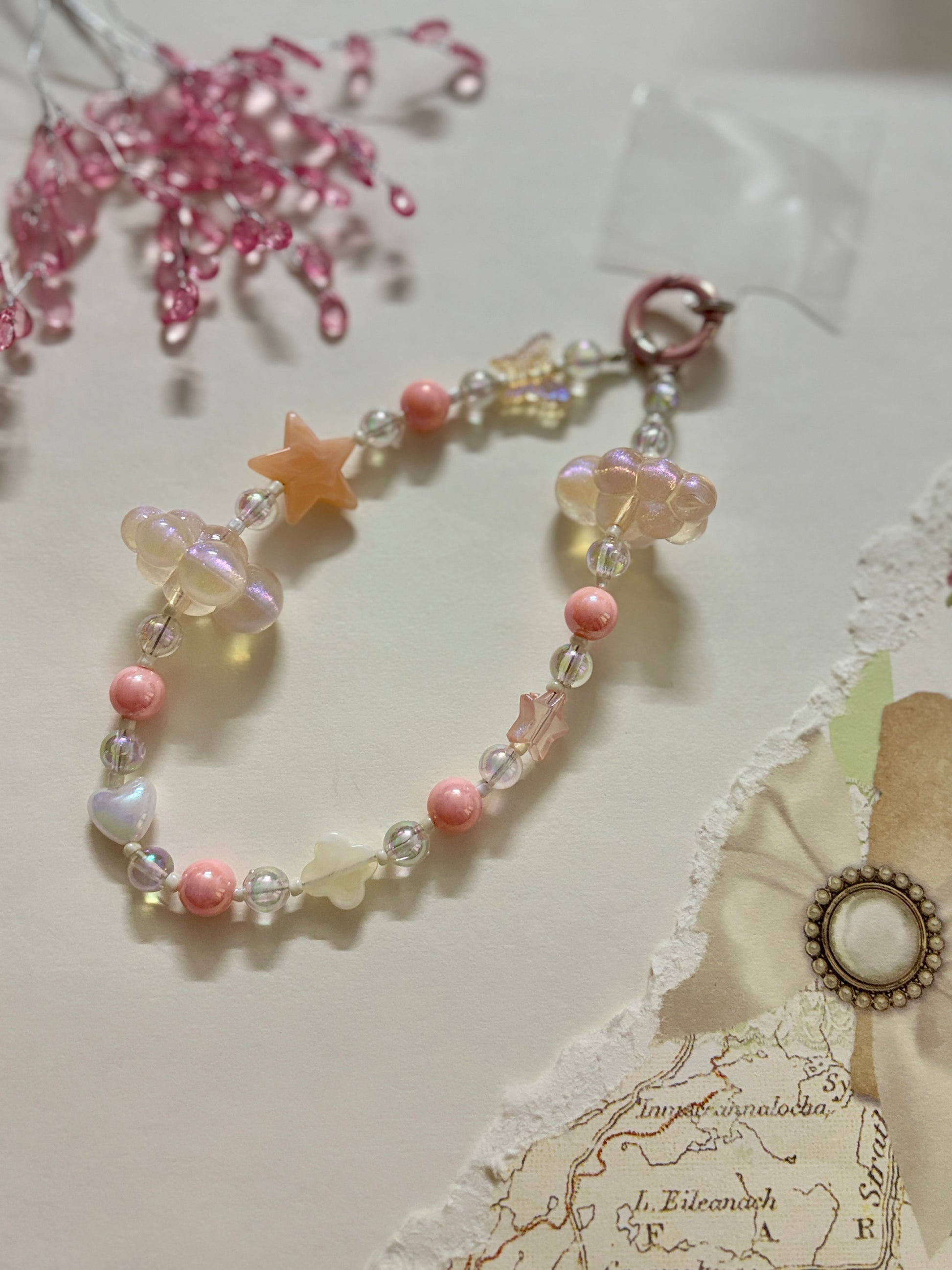 Aesthetic beaded phone charm featuring translucent clouds, a navy star, pastel beads, and butterfly accents, arranged in a dreamy celestial theme.