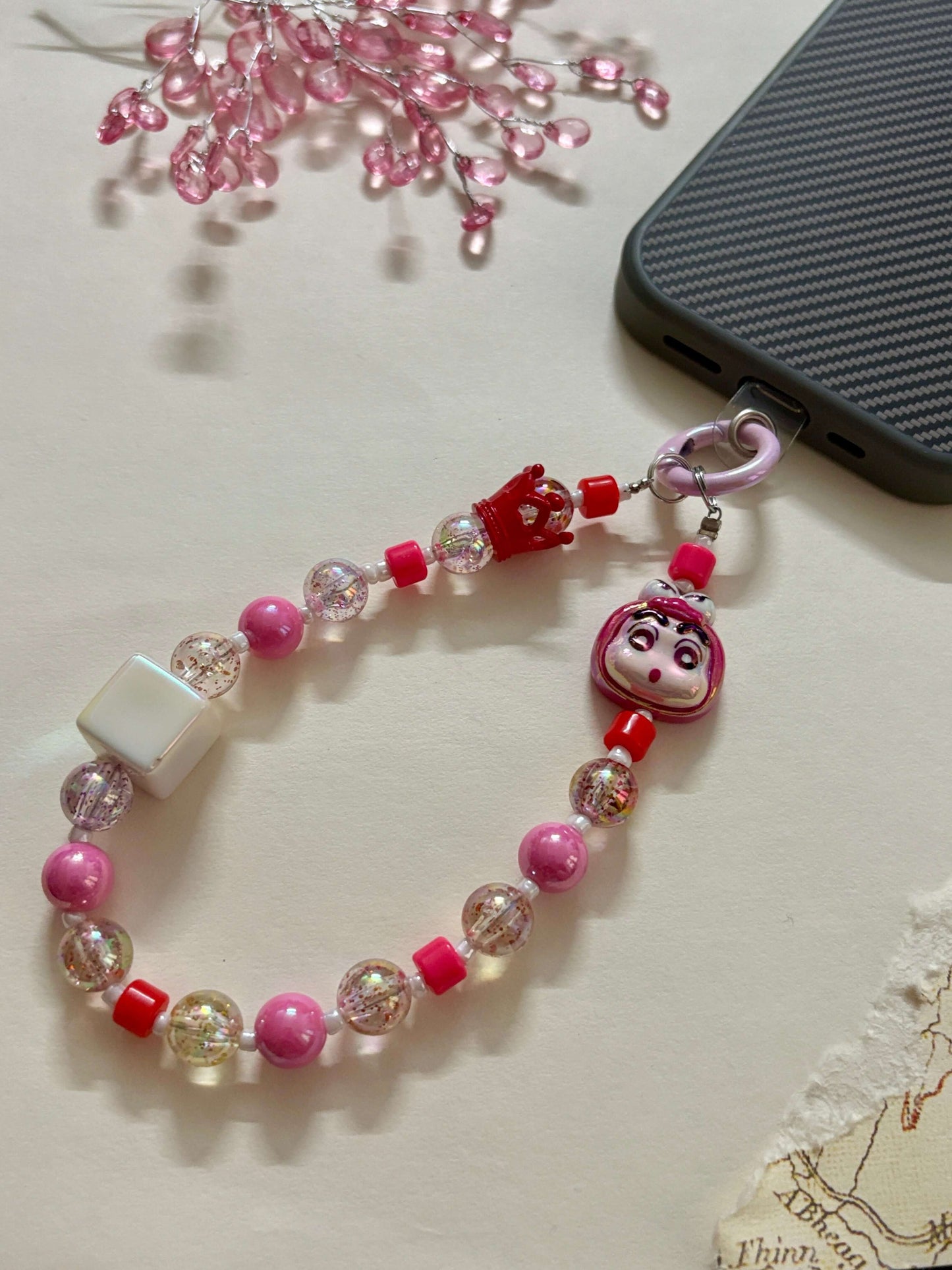 A handmade phone charm strap featuring glitter-filled resin beads, blue and white accents, a Shin Chan character charm, and a secure loop for attaching to phone cases or bags.
