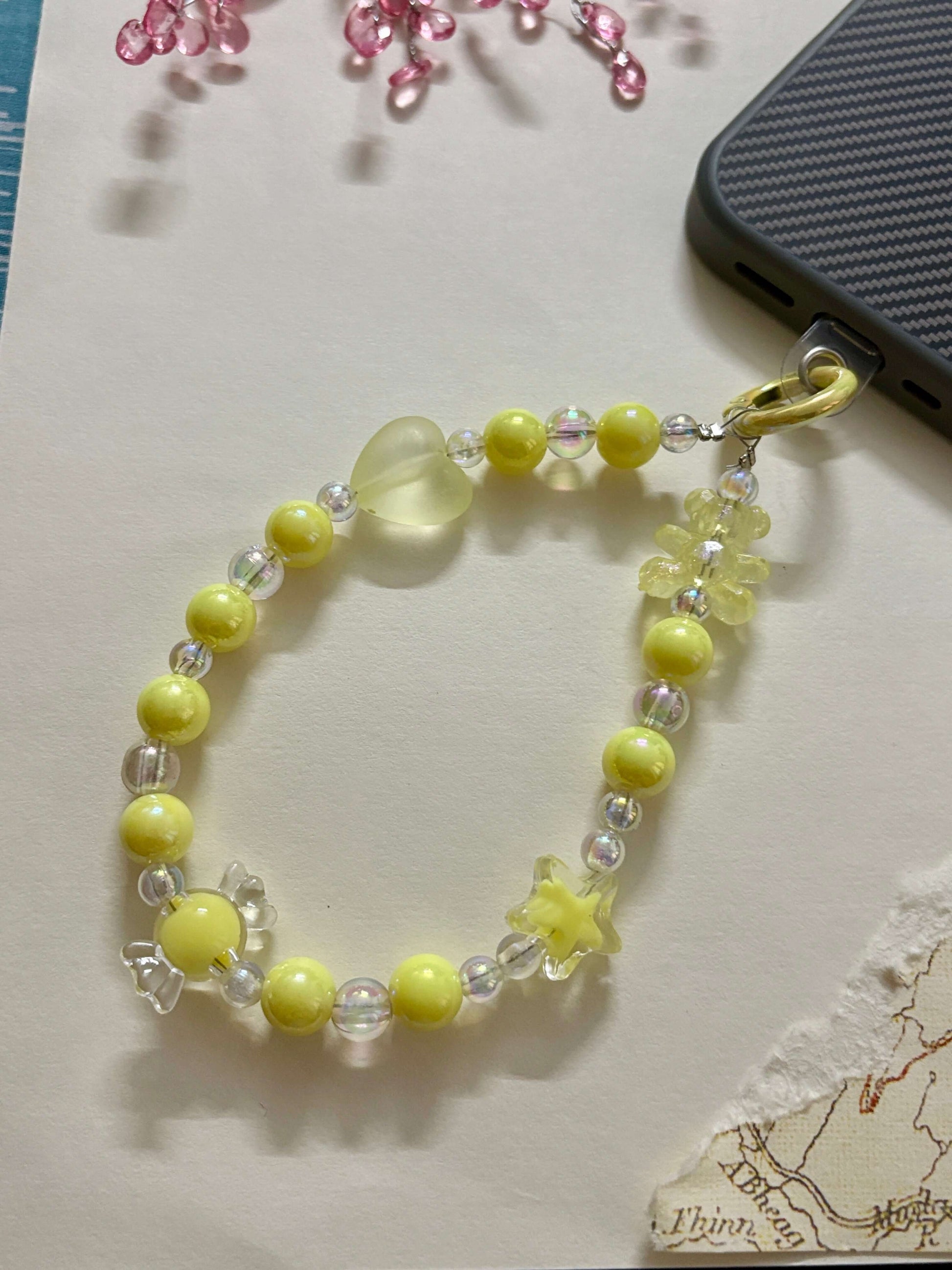 Beaded phone charm with heart, star, and teddy bear accents, designed to hang from a mobile device; features pearl and translucent beads for a cute and playful look.